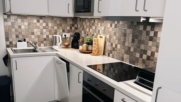 A modern kitchen with white cabinetry, a microwave, a stove, and a tiled backsplash. - Bright and Cozy 40 m² Apartment at Prague 7 (Prague)