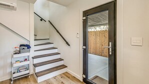 Eine Treppe mit Handlauf, eine Tür mit Fensterteil und eine weiße Wand mit Lichtschalter.