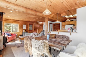 A rustic cabin interior with a wooden dining table, a sofa, and a kitchen area.