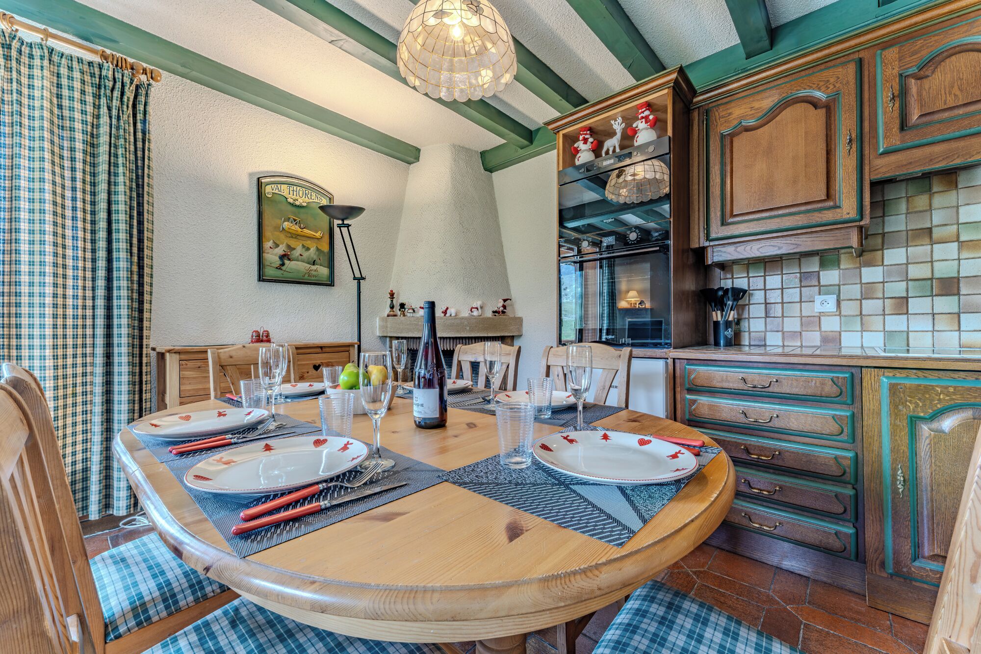 Ein Essbereich mit einem Holztisch, gedeckt für vier Personen, umgeben von Stühlen. Es gibt eine Küchenzeile mit Holzschränken und einer gefliesten Spritzschutzwand.