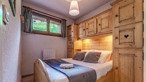 A bedroom with a wooden bed, a window with curtains, and wooden cabinets. - Chalet Niverolles (Les Belleville)