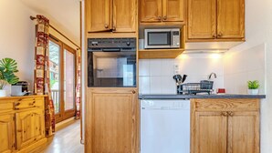 A kitchen with wooden cabinets, a microwave, an oven, and a dishwasher. - Chalet Niverolles (Les Belleville)