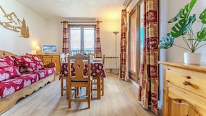 A cozy room with a bed, a dining table, chairs, and a large window with curtains. - Chalet Niverolles (Les Belleville)