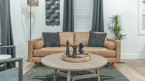Ein modernes Wohnzimmer mit einer braunen Ledersofa, einem runden Couchtisch mit Dekoration, einer Stehlampe und einem Wandbild.