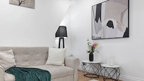 Ett minimalistiskt vardagsrum med en beige soffa, en svart golvlampa och abstrakt väggkonst.