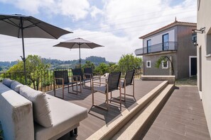 An outdoor terrace with a sofa, chairs, and umbrellas, overlooking a scenic landscape. - Holiday Home 'Picturesque in Northern Portugal' with Private Garden, Balcony and Wi-Fi (Braga)