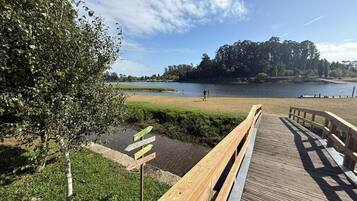 Un paseo marítimo de madera que conduce a un lago, con zonas de césped y árboles al fondo.