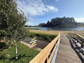 A wooden boardwalk leading to a lake with grassy areas and trees in the background. - Holiday Home 'Picturesque in Northern Portugal' with Private Garden, Balcony and Wi-Fi (Braga)