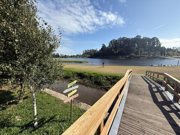 A wooden boardwalk leading to a lake with grassy areas and trees in the background. - Holiday Home 'Picturesque in Northern Portugal' with Private Garden, Balcony and Wi-Fi (Braga)