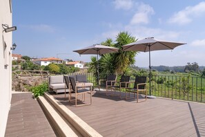 A deck with outdoor furniture and umbrellas, overlooking a green landscape with houses. - Holiday Home 'Picturesque in Northern Portugal' with Private Garden, Balcony and Wi-Fi (Braga)
