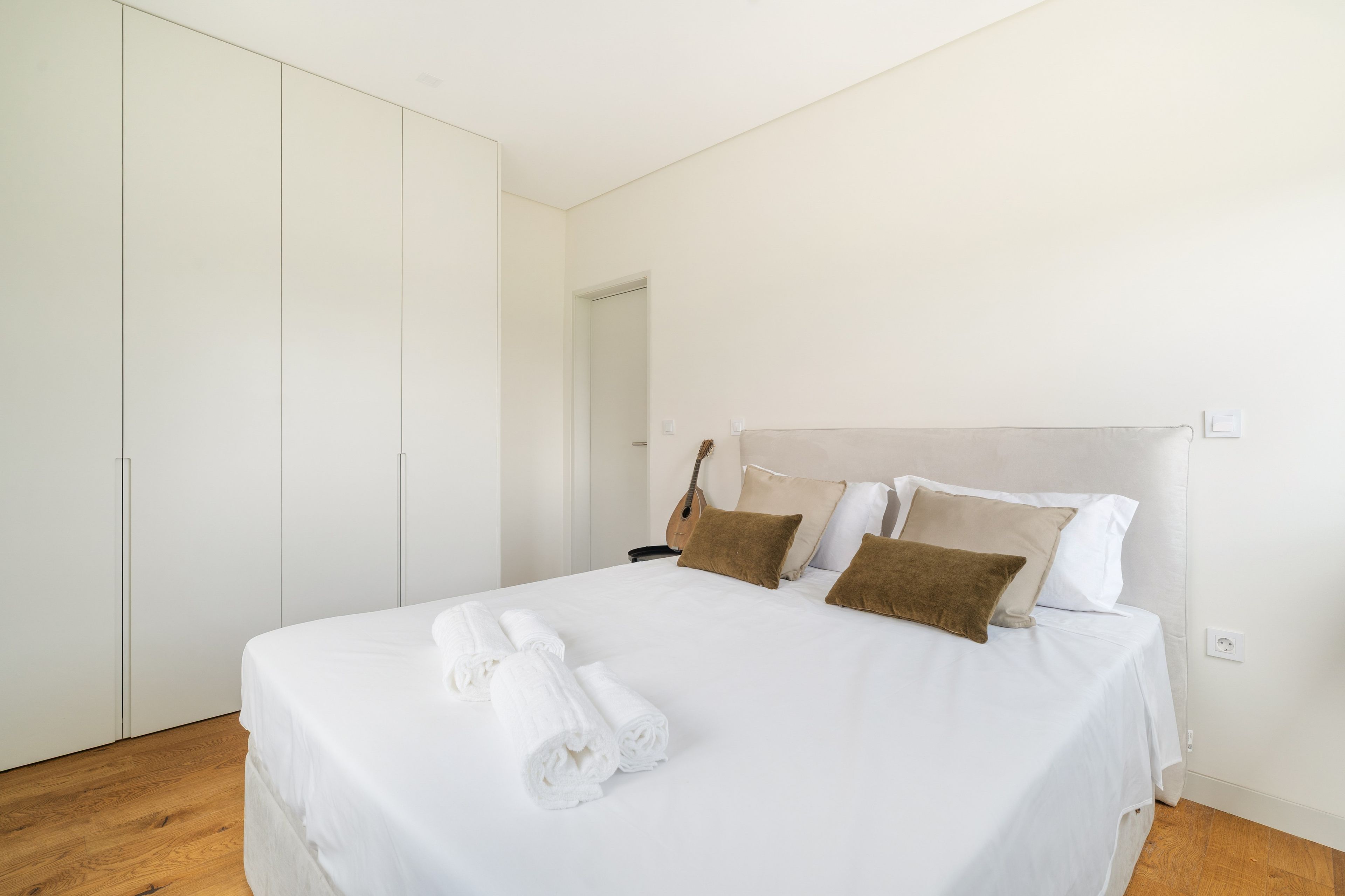 Ein ordentlich bezogenes Bett mit weißen Leinen und aufgerollten Handtüchern, ein Holzboden und ein großer Kleiderschrank.