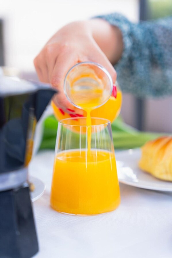 A hand pouring orange juice into a glass.