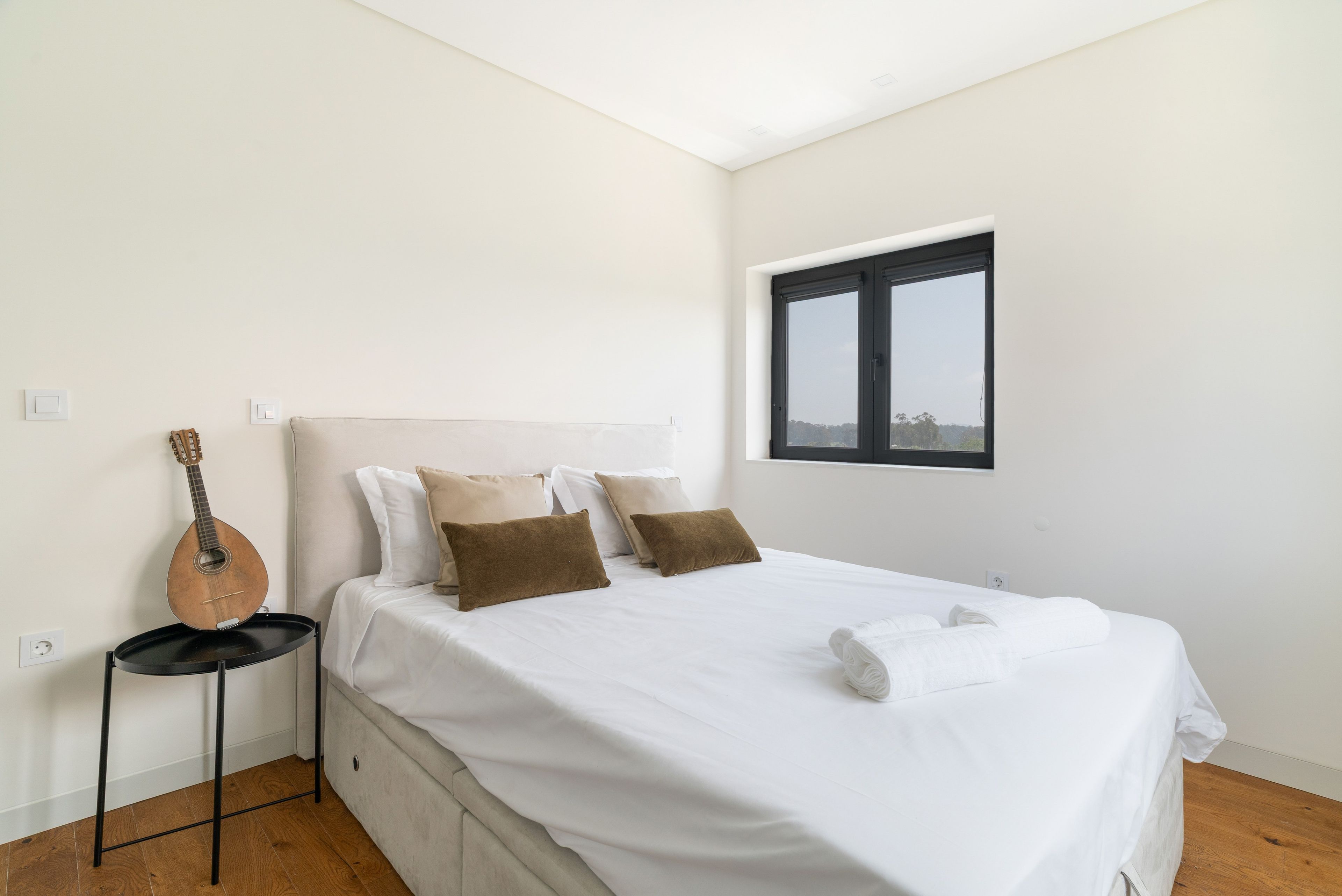 A bedroom with a bed, pillows, a guitar, a window, and a view.