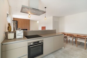 A modern kitchen with a built-in oven, a dining table with chairs, and a large window.