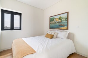 A bedroom with a bed, a window, and a painting on the wall.