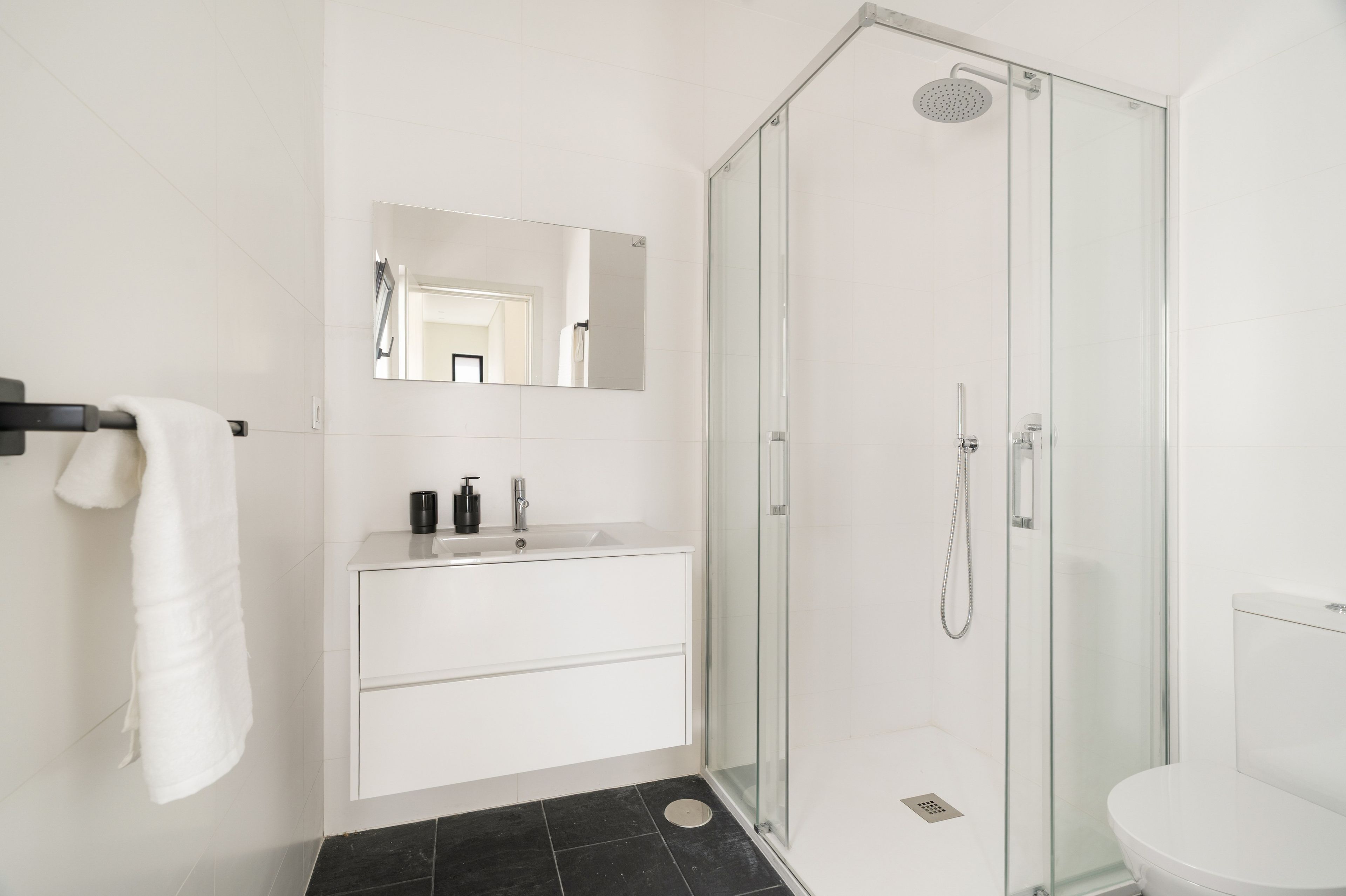 Un baño moderno con ducha envuelta en cristal, un lavabo blanco con espejo y un inodoro blanco.