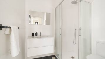 Un baño moderno con ducha envuelta en cristal, un lavabo blanco con espejo y un inodoro blanco.