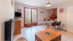 Een woonkamer met een televisie, een houten kast, een eettafel met stoelen en een trap naar een hoger niveau.