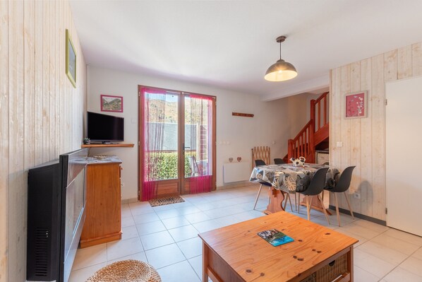 A living room with a TV, wooden cabinet, dining table with chairs, and a staircase leading to another level.