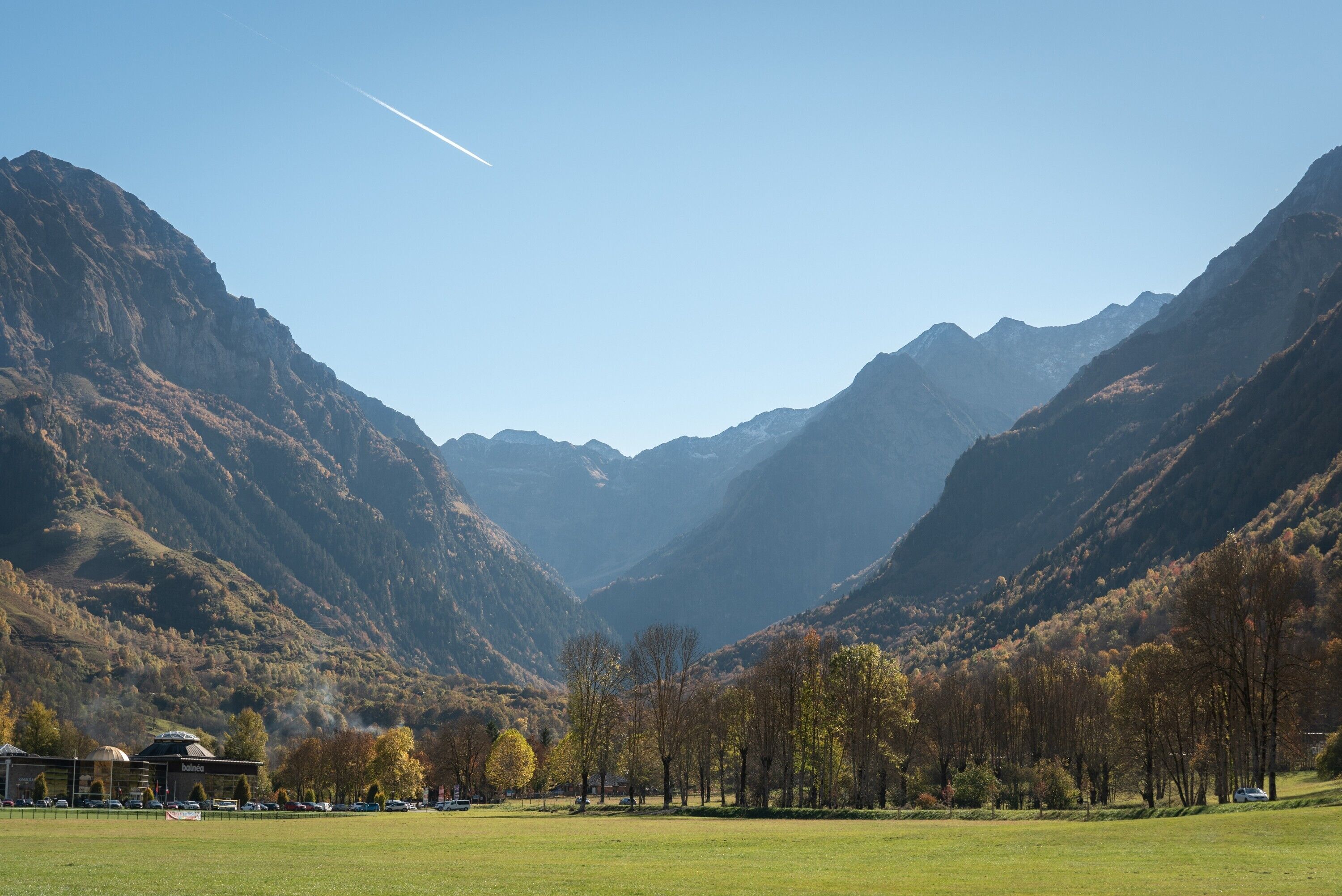 Eine gebirgige Landschaft mit blauem Himmel, einem Gebäude mit Kuppeldach und einem grünen Feld im Vordergrund.