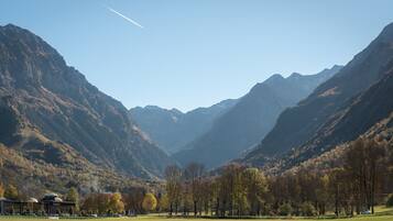 Eine gebirgige Landschaft mit blauem Himmel, einem Gebäude mit Kuppeldach und einem grünen Feld im Vordergrund.