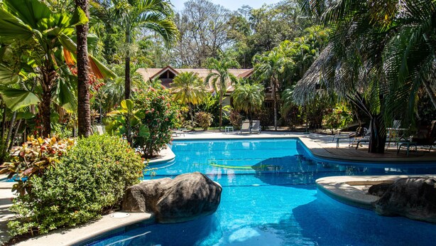 A swimming pool surrounded by tropical vegetation and a building with a tiled roof. - Quiet Oasis | Peaceful Villa in Nosara (Nosara)