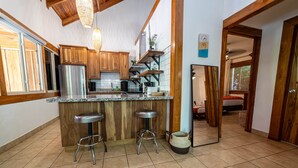 A kitchen with wooden cabinets, a stainless steel refrigerator, a granite countertop, and two bar stools. - Quiet Oasis | Peaceful Villa in Nosara (Nosara)