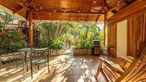 A covered patio area with wooden flooring, metal furniture, and a variety of tropical plants. - Quiet Oasis | Peaceful Villa in Nosara (Nosara)
