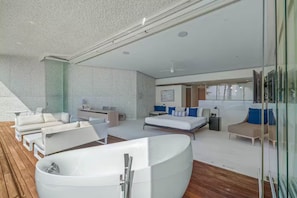 Een moderne, ruime woonkamer met een groot bad, een zithoek en een bed met blauwe kussens.