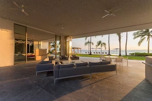 Een moderne buitenlounge met uitzicht op de oceaan, ingericht met banken en stoelen, en een glazen wand met uitzicht op het strand.