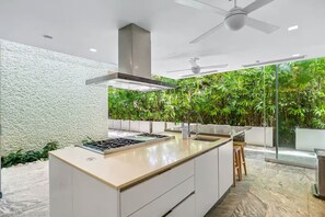 Een moderne keuken met een centraal eiland, ingebouwde apparatuur en uitzicht op weelderige begroeiing door grote ramen.