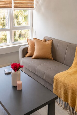 Ein Wohnzimmer mit einer Couch, Kissen, einer Vase mit Blumen, einer Kerze und einer Decke auf einem Tisch.