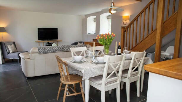 A dining area with a table set for four, a sofa, a TV, and a staircase. - The Dovecote, Llechryd (Llechryd)