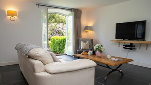 A modern living room with a sofa, a coffee table, a TV, and a view of a garden. - The Dovecote, Llechryd (Llechryd)