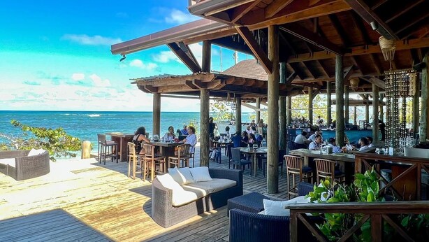 An outdoor dining area with wooden tables and chairs, overlooking a body of water.