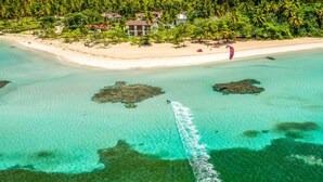 An aerial view of a coastal resort with clear turquoise waters, a sandy beach, and lush greenery.