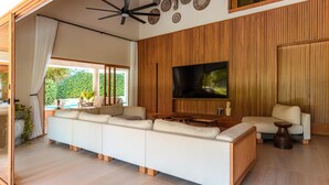 A modern living room with a large TV, wooden paneling, a sofa, and a ceiling fan.