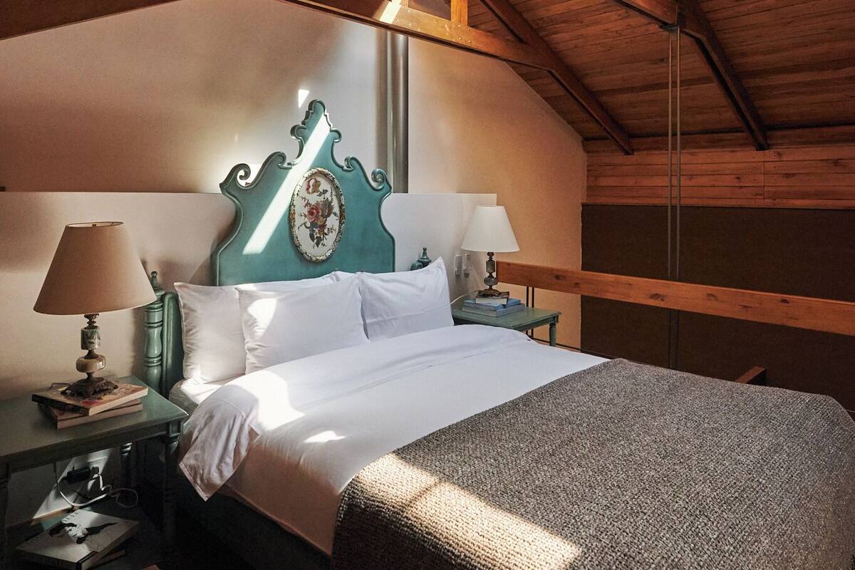 Una camera da letto con soffitto in legno, un letto con lenzuola bianche, due comodini con lampade e una testiera decorativa.