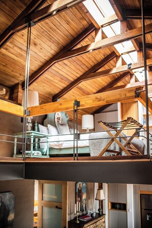 A loft bedroom with a sloped ceiling, wooden beams, a bed with pillows, a hanging chair, and a view of the lower level. - Casa Santa Clara-Colonial Boutique Hotel (Quito)