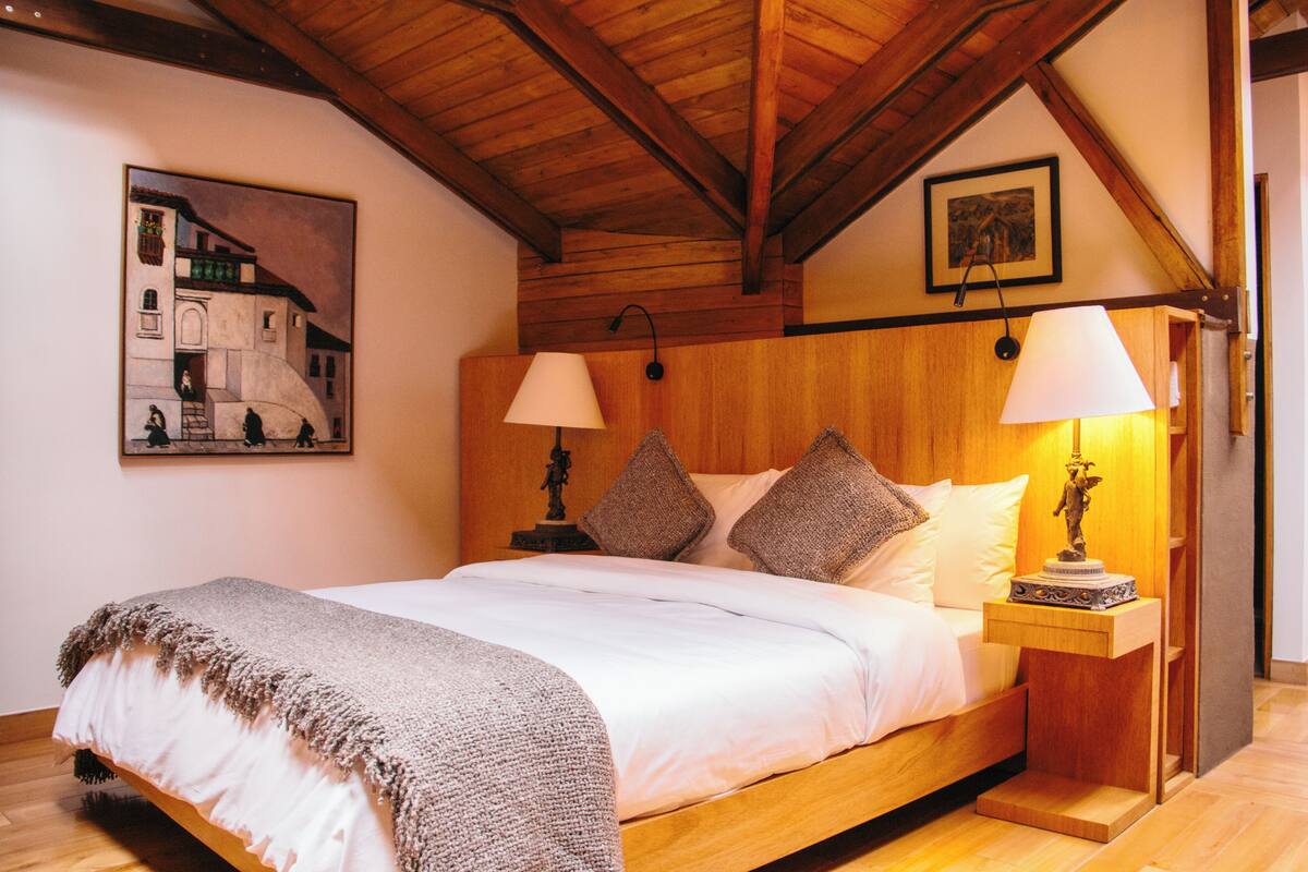 Una camera da letto con un letto in legno, due lampade ai comodini, un tavolino e un quadro appeso al muro.