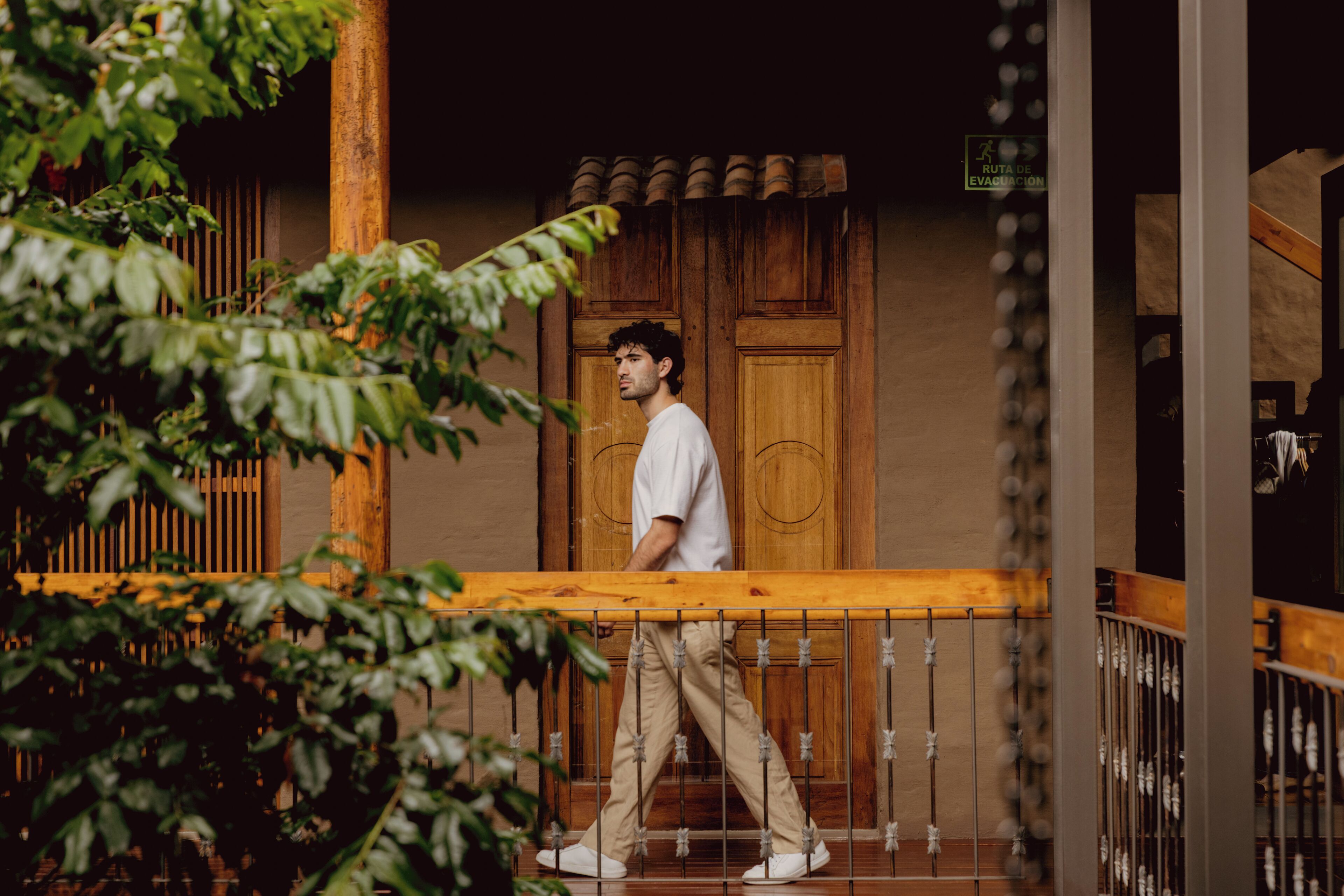 A person walking on a wooden balcony with a railing, surrounded by greenery.
