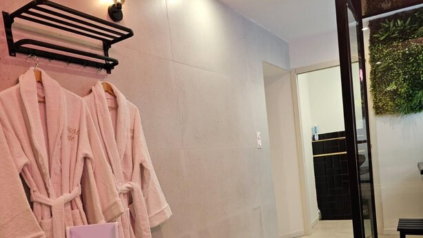 A bathroom with a bathtub, a towel rack with robes, and a small wooden tray.