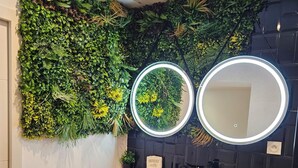 A bathroom with two stone sinks, a black vanity, a mirror with a light, and a green vertical garden.