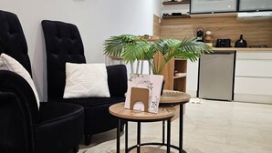 A modern living room with two black armchairs, a small round table with a plant, and a kitchen in the background.