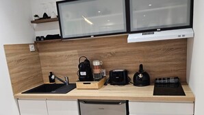 A compact kitchen with a dishwasher, a coffee machine, a kettle, and a toaster.