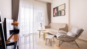 A modern living room with a sofa, a rocking chair, a TV, and a small table with a vase of flowers. - Gin House - Golden Mansion Apartment Phu Nhuan District (Ho Chi Minh City)