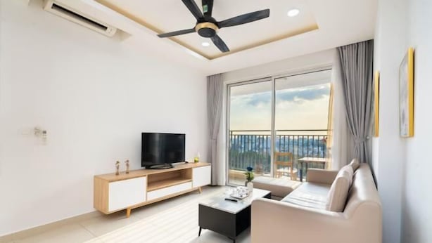 A modern living room with a flat-screen TV, a sofa, a coffee table, and a balcony with a view. - Gin House - Golden Mansion Apartment Phu Nhuan District (Ho Chi Minh City)