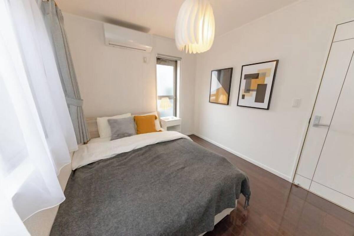 A bedroom with a bed, a window, a wall-mounted air conditioner, and a door.