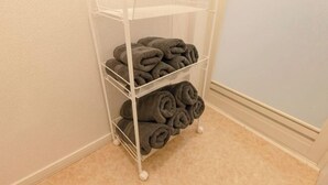 A white metal shelf unit with three tiers, each holding neatly rolled towels. - Iris Tokyo ２ (Tokyo)