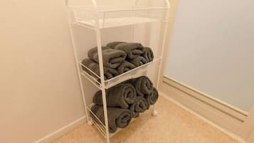 A white metal shelf unit with three tiers, each holding neatly rolled towels.